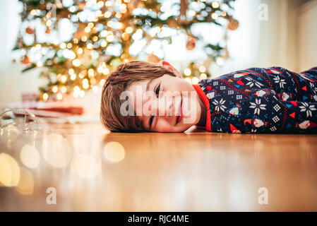 Sorridente ragazzo disteso sul pavimento nella parte anteriore di un albero di Natale Foto Stock