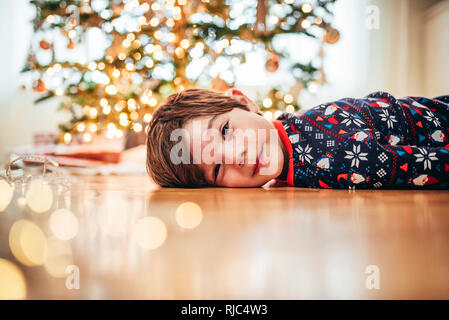 Sorridente ragazzo disteso sul pavimento nella parte anteriore di un albero di Natale Foto Stock