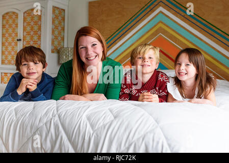 La madre ed i suoi tre figli giacente su un letto di sorridere Foto Stock