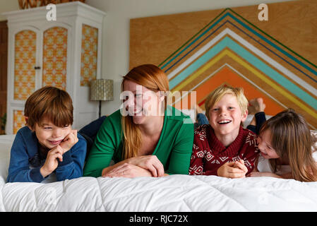 La madre ed i suoi tre figli giacente su un letto di sorridere Foto Stock