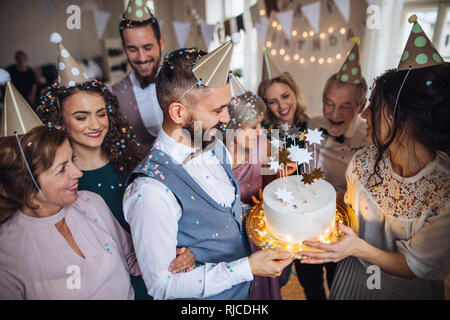 Un ritratto di famiglia multigenerazionali con una torta su una piscina festa di compleanno. Foto Stock