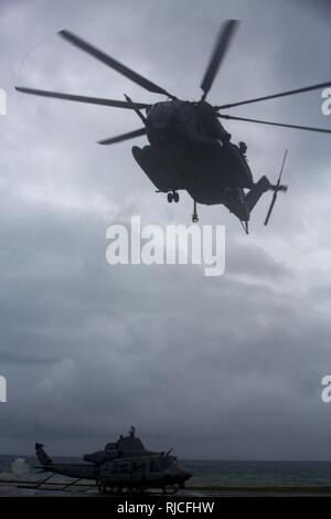 Un U.S. Marine CH-53E "Super Stallion" elicottero con il primo velivolo Marina Wing e la terza Marine Logistics Group, elicottero Supporto offload del team un UG-1Y "veleno" Huey elicottero dopo un atterraggio di emergenza a Uruma Beach, Base Navale spiaggia bianca, Okinawa, in Giappone. 8 gennaio 2018. La UH-1Y elicottero atterrato su Ikeijina una piccola isola a Okinawa principale dell'isola, dopo le indicazioni che il rotore principale è in movimento a pericolosamente ad alta velocità. Nessuno è stato ferito nell'incidente. Foto Stock