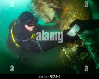 Stati Uniti Costruzione navale elettricista di seconda classe Dailey Timoteo, assegnato alla costruzione subacquea Team (UCT) 2, avvolge esplosivo del nastro di taglio (ECT) intorno a una pila durante un tuffo al comandante, le attività della flotta Sasebo (CFAS), Giappone, gen. 16, 2018. UCT-2 fornisce la costruzione, ispezione, manutenzione e riparazione di subacquea e waterfront strutture a sostegno della flotta del Pacifico. Foto Stock