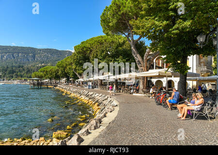 GARDA, Italia - Settembre 2018: PPeople seduti sui sedili sulla riva del lago di Garda sul Lago di Garda. Foto Stock