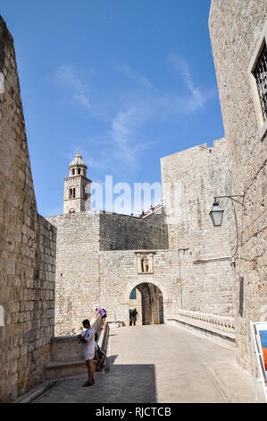 I turisti nella parte anteriore della parte interna del cancello PLOCE, parte della cinta muraria della città, con una vista del campanile del monastero domenicano dietro Foto Stock