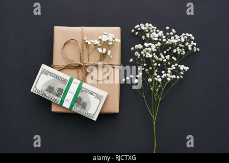 Il modo migliore per presentare per i vostri cari. In casa confezione regalo in kraft carta marrone decorato con fiori e il denaro come un regalo su sfondo scuro Foto Stock