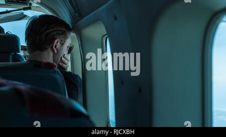 Una foto di un giovane uomo che indossa gli occhiali da sole guardando fuori dalla finestra del Cessna Grand Caravan durante il volo da San Jose a Drake Bay Foto Stock