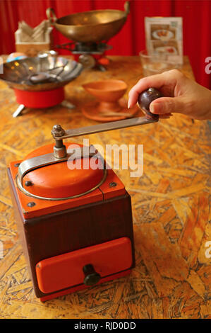 Donna di macinazione a mano i chicchi di caffè in una vibrante colore portatile retrò macinino da caffè per caffè fatti in casa Foto Stock