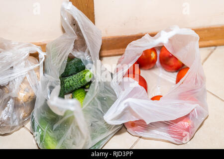 Vista dettagliata del fresco verde drogheria produrre sacchetti di plastica con cetrioli e pomodori patate sul pavimento di cucina da supermercato o mercato degli agricoltori dopo sho Foto Stock