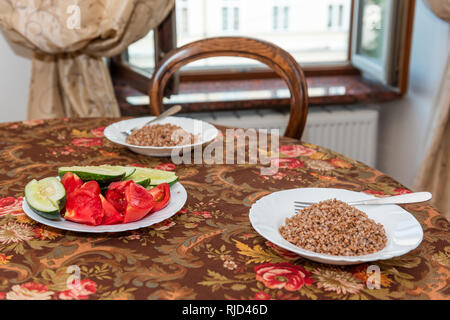 Rustico in legno vintage tavolo antico tovaglia e finestra in Ucraina o in Russia con la piastra di fresche verdure tagliate a fette, cetrioli e pomodori e buckw Foto Stock