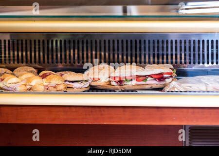 La visualizzazione di molte grandi panini dietro il vetro della finestra del negozio ripieni di prosciutto formaggio e pomodori in Italia con cornetti e panini Foto Stock