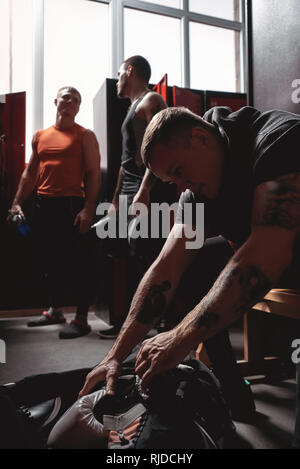 Muscoloso giovane atleta boxer di capi di abbigliamento sportivi come ottenere i guantoni al di fuori della sua borsa in dark palestra spogliatoi. Messa a fuoco selettiva Foto Stock