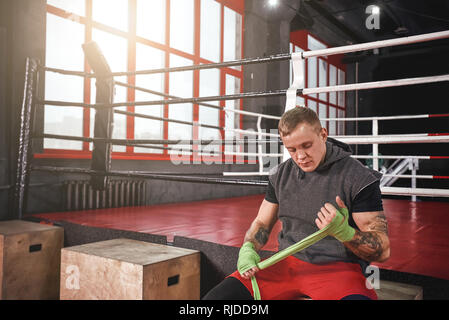 Preparazione di combattimento. Fiducioso athletic tatuato uomo mani di incarto con bende di verde. Forti mani e pugno pronto per la lotta Foto Stock