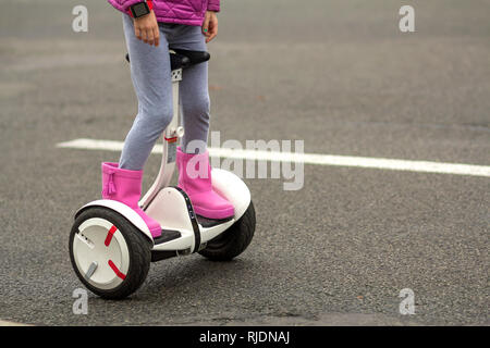 Close-up di bambino ragazza gambe in rosa luminoso stivali di gomma equitazione segway sulla soleggiata strada asfaltata spazio copia dello sfondo. La moderna tecnologia, bambini safet Foto Stock