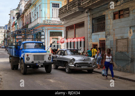 Scena su una tipica strada a l'Avana a Cuba. Persone locali per lo shopping e a piedi lungo e una vecchia vettura americana e un carrello sovietica la guida su strada Foto Stock