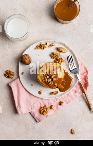 Una sana prima colazione, stack di american pancake con caramello souse e dadi a piastra bianca con una forchetta e tovagliolo rosa, vista dall'alto Foto Stock