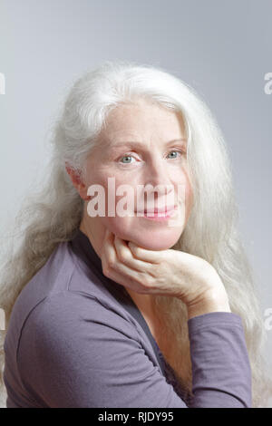 Ritratto di un attraente donna matura con belle lunghi capelli bianchi davanti a uno sfondo grigio. Foto Stock