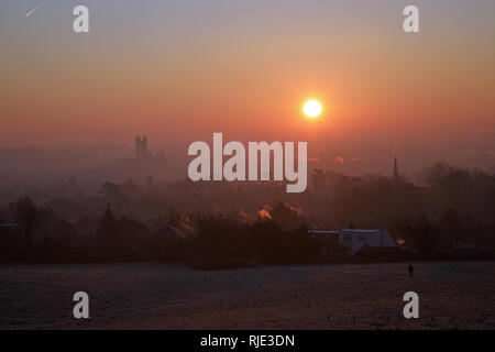 Alba sul Canterbury in un freddo, croccante mattina di gennaio con aeromobili sentieri di vapore nel cielo e un camminatore solitario in primo piano. Foto Stock