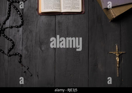 Aprire il libro della Bibbia e del Crocifisso su tavola scuro, vista dall'alto. Piano immagine di laici del Nuovo Testamento, la croce e il rosario sul vecchio sfondo nero Foto Stock