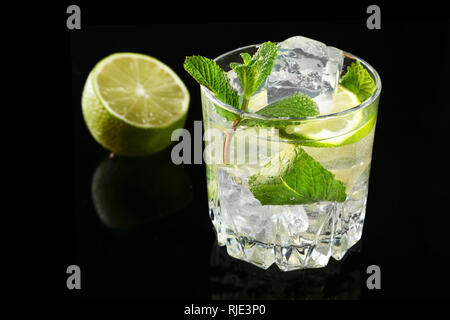 Bicchiere di cocktail con rum, calce, cubetti di ghiaccio e foglie di menta su Black mirror sfondo. Foto Stock
