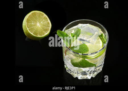 Bicchiere di cocktail con rum, calce, cubetti di ghiaccio e foglie di menta su Black mirror sfondo. Foto Stock