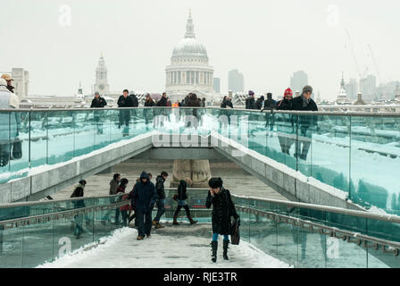 Il Millennium Bridge ricoperta di neve con St Pauls Cathedral in background visto attraverso la caduta di neve; persone che fanno la loro strada attraverso il ponte. Foto Stock