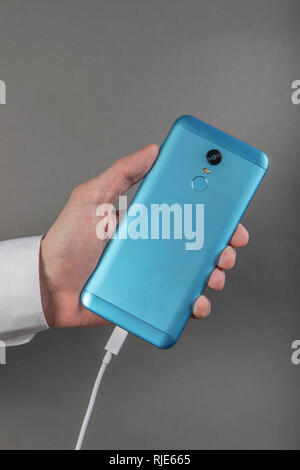 Mano d'uomo tenendo lo smartphone con il cavo usb Foto Stock