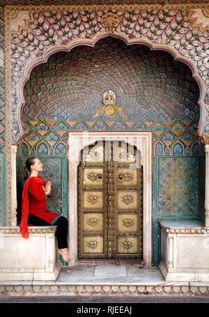 La donna in sciarpa rossa seduta vicino Lotus gate nel palazzo di città di Jaipur, Rajasthan, India Foto Stock