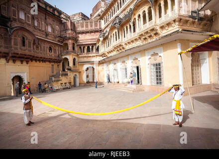 JODHPUR, Rajasthan, India - 08 Marzo 2015: due uomini nella tradizionale panno Rajasthan che mostra come rendere turbante dal panno giallo nella parte anteriore del gruppo di t Foto Stock