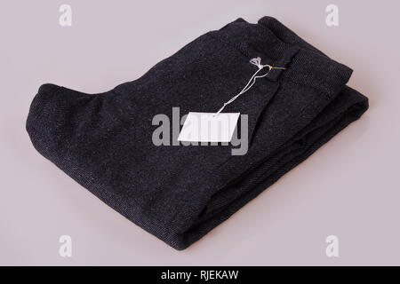 Organici grigio scuro pantaloni. Pantalone pila su uno sfondo bianco. Abbigliamento tag. Carta bianca prezzo tag etichetta Foto Stock