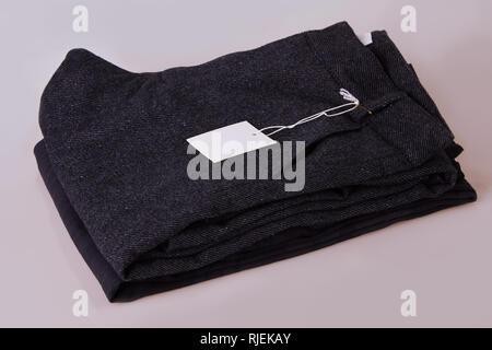 Organici grigio scuro pantaloni. Pantalone pila su uno sfondo bianco. Abbigliamento tag. Carta bianca prezzo tag etichetta Foto Stock