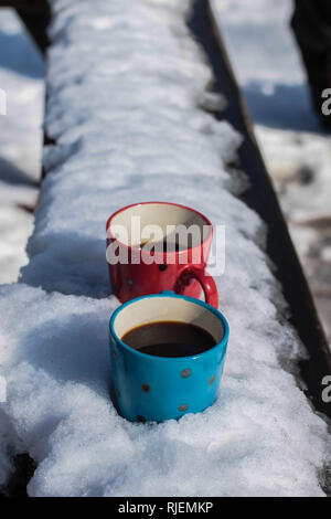 Due tazze di caffè e una ciambella sulla panchina coperta di neve Foto Stock