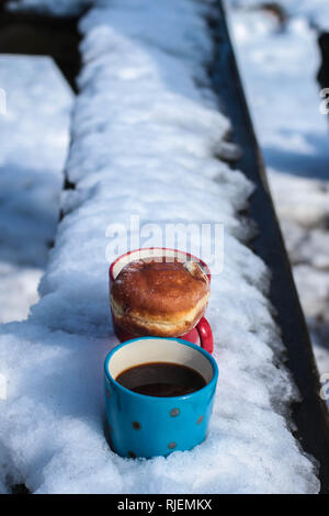 Due tazze di caffè e una ciambella sulla panchina coperta di neve Foto Stock