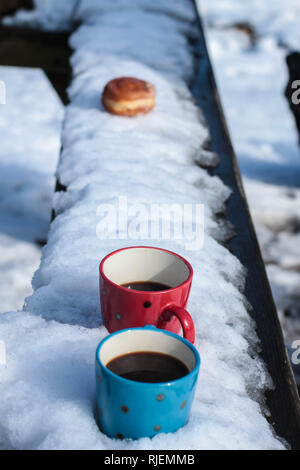 Due tazze di caffè e una ciambella sulla panchina coperta di neve Foto Stock