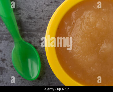 Tettuccio di chiudere la vista di un piccolo giallo ciotola riempita con la salsa di mele e un cucchiaio di verde a lato su sfondo grigio. Foto Stock