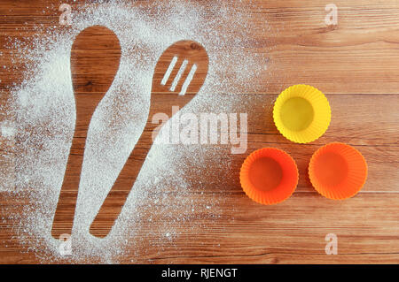 Eventuali fuoriuscite di farina a fontana sul tavolo. Conformati a guisa di cucchiaio imprint nella farina e torta stampi. Legno marrone dello sfondo. Foto Stock