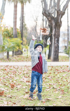 Bambino vestito in abiti caldi gettando caduto foglie di autunno in aria Foto Stock