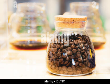 I chicchi di caffè in un contenitore di vetro sul tavolo di legno Foto Stock