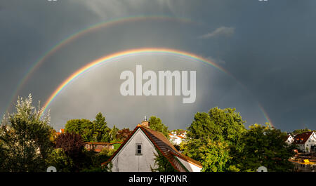 Full doppio arcobaleno su drammaticamente illuminati case in un grigio scuro sky Foto Stock