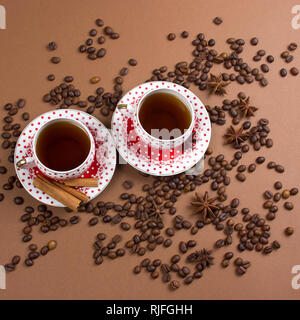 Due piccante di caffè nero polka dot tazze e i chicchi di caffè pasticcio su sfondo marrone squae immagine Foto Stock