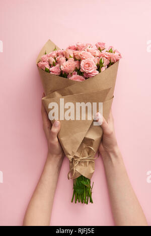 Ritagliato colpo di mani femminili holding bouquet di bellissime rose rosa avvolto in carta artigianale in rosa Foto Stock