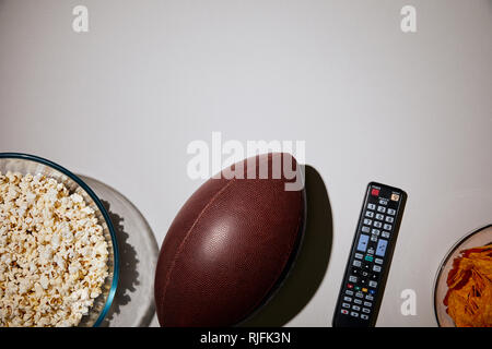 Vista superiore del popcorn nella ciotola vicino a sfera e il controllo remoto su sfondo bianco Foto Stock
