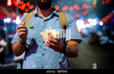 Man aventi gelato rotoli nella notte asiatica mercato alimentare Foto Stock