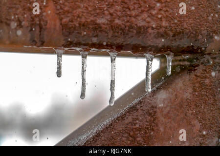 Fila di ghiaccioli su binari di metallo di un ponte Foto Stock