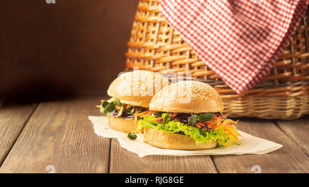 Hamburger Vegetariano fatto da fresche ciambelle di sesamo e verdure crude e giovani germogli picnic rustico in legno sfondo. Foto Stock