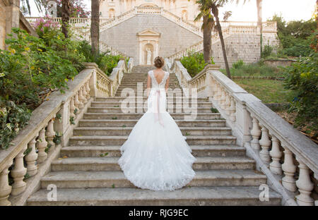 Grazioso sposa salite le scale di pietra in un abito da sposa Foto Stock