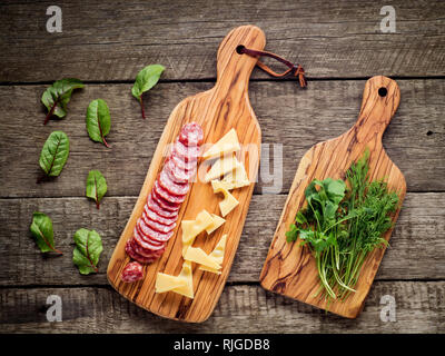 Formaggi e salumi su cucina di bordo su sfondo rustico. Vista da sopra con copia di spazio e di erbe aromatiche. Foto Stock