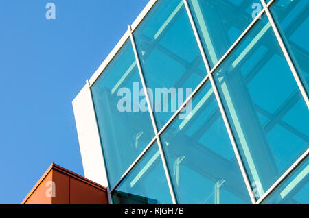 Forme geometriche di un moderno edificio di vetro e pietra contro il cielo blu chiaro Foto Stock