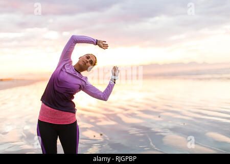 Giovani femmine pareggiatore di stretching prima di correre sulla spiaggia di sunrise Foto Stock