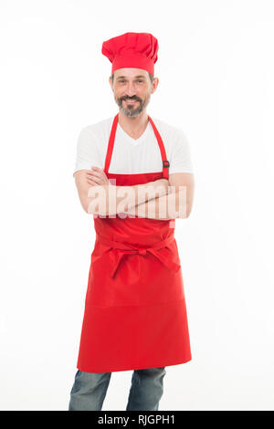 Tenere le braccia incrociate con fiducia. Barbuto uomo maturo in chef hat e grembiule. Senior cucinare con la barba e baffi indossando grembiule di bib. Coppia capo cuoco in cucina rosso grembiule. Cucina casalinga. Foto Stock